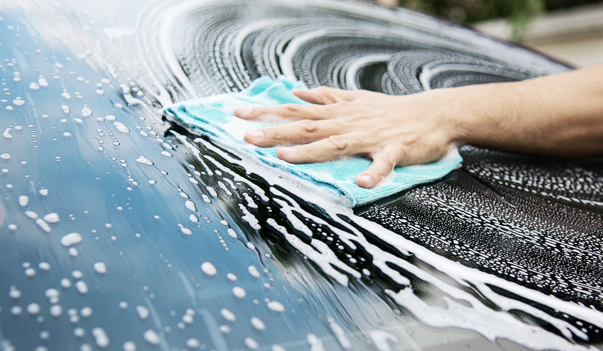 Person cleaning a car windshield with a blue microfiber cloth, surrounded by soap suds, emphasizing auto glass maintenance for Florida drivers.