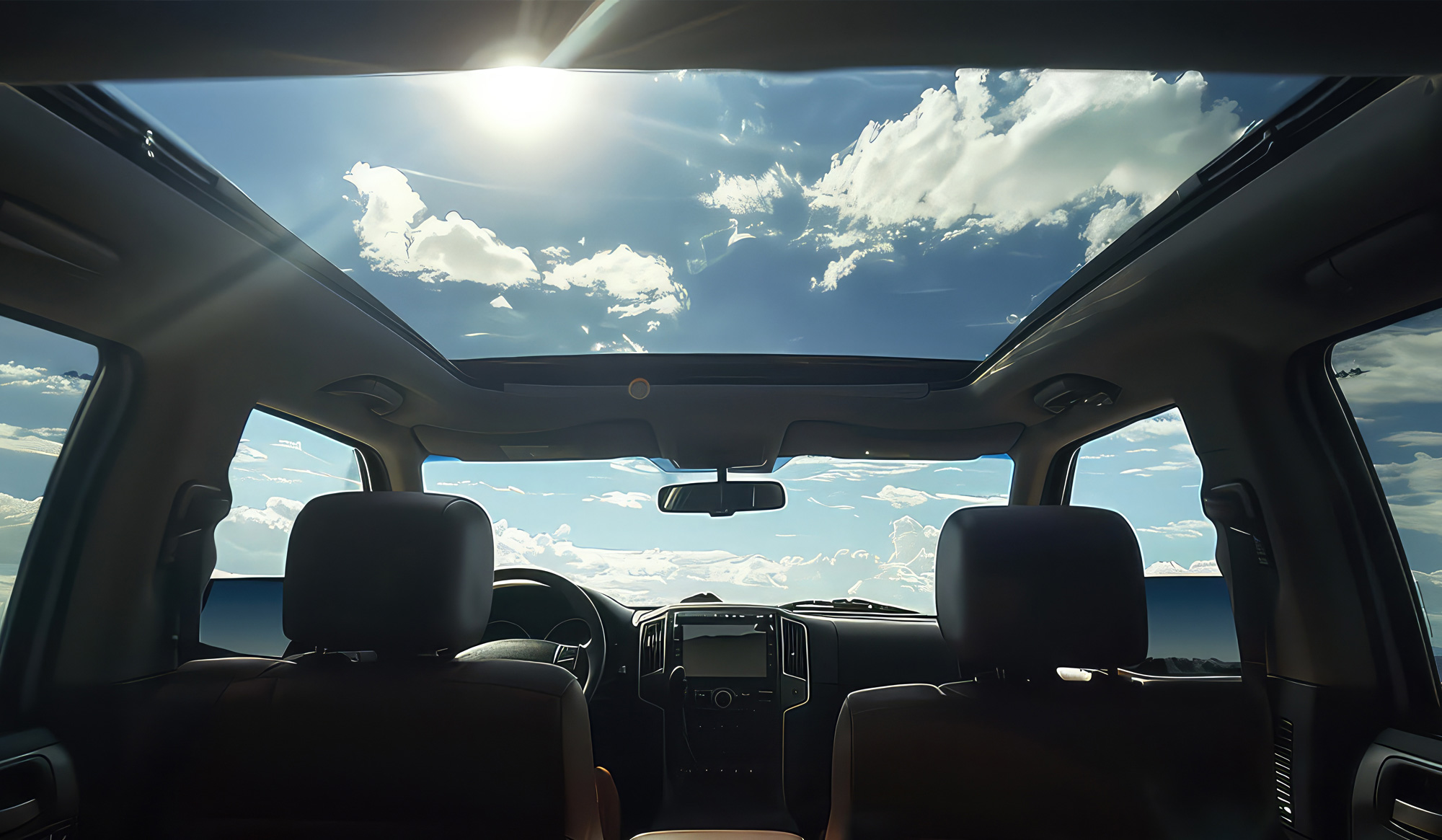 Interior view of a vehicle showcasing a panoramic glass roof, bright sky, and clouds, emphasizing modern automotive design and features.