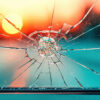 Windshield chip with spider web cracks against a blurred sunset background, highlighting the importance of auto glass maintenance for Florida drivers.