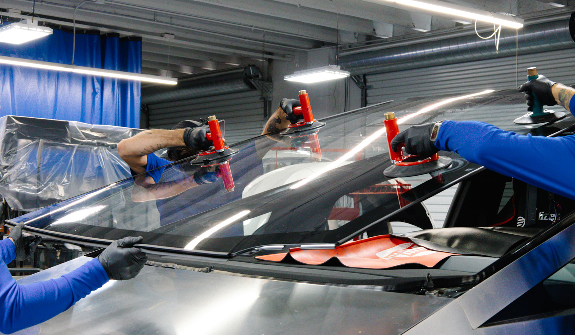 Technicians replacing a windshield using suction cups in an auto glass repair shop, highlighting the importance of professional windshield replacement services in Florida.
